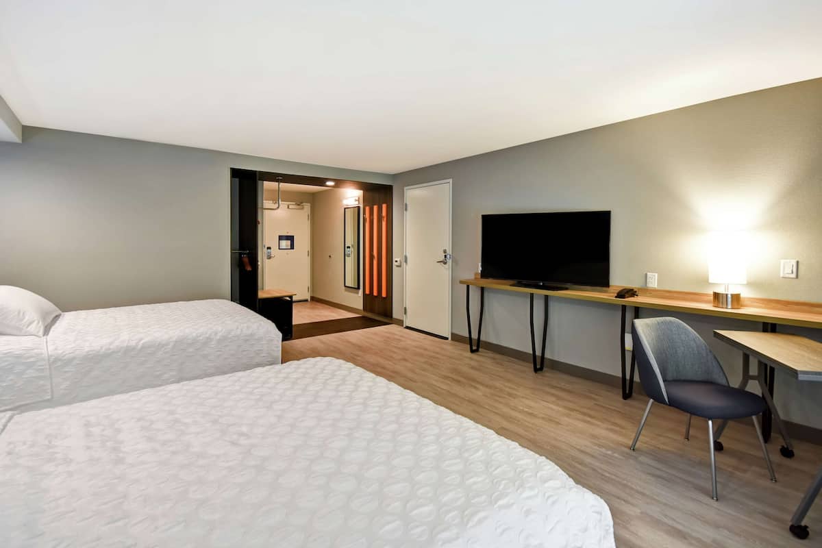 Een hotelkamer met twee bedden, een bureau met stoel, een televisie en een spiegel.