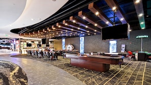 Un hall d’hôtel moderne doté d’un espace salon aux lignes courbes, d’un bar et d’une table de roulette.