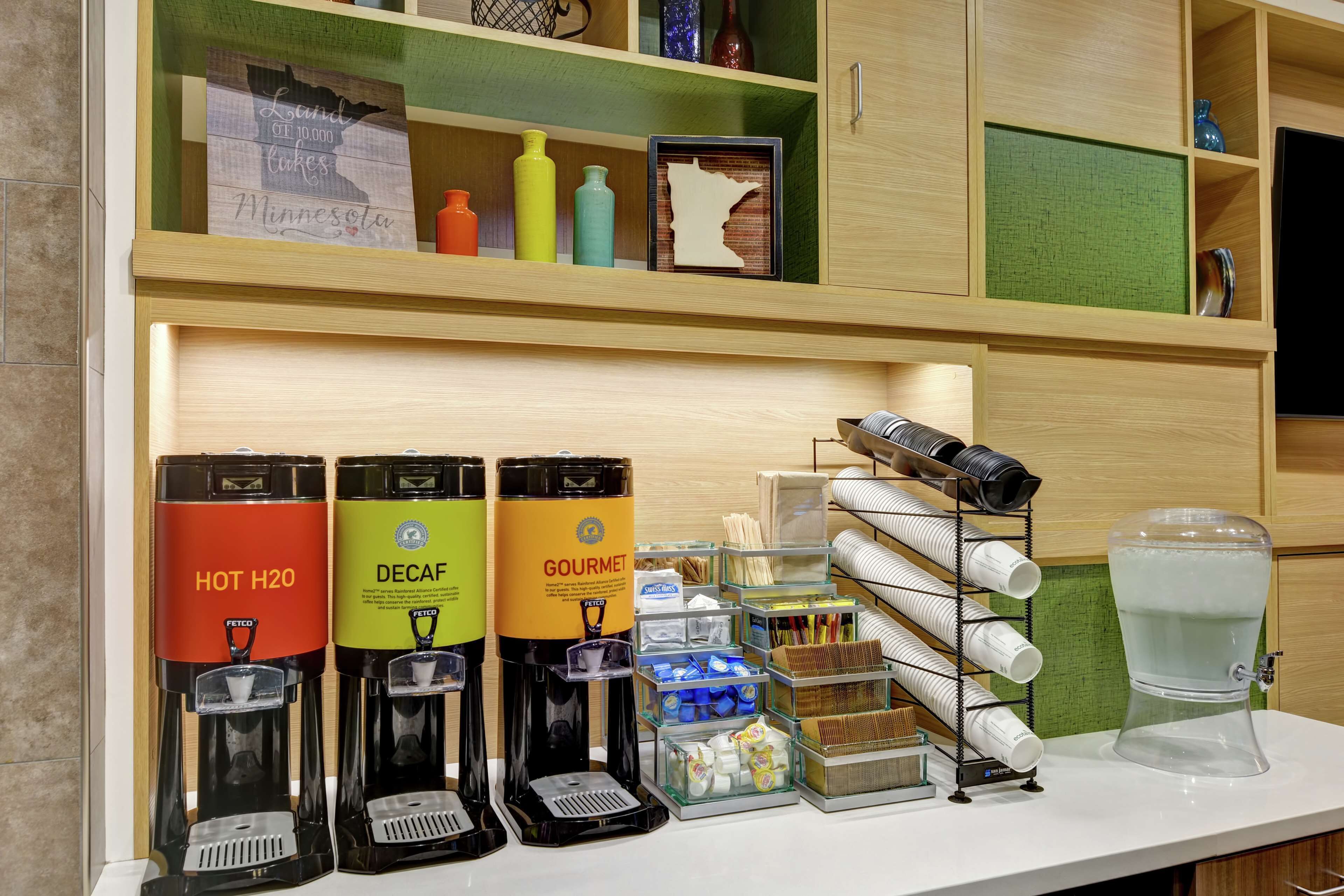 Un espace dédié au café, équipé de trois distributeurs de boissons étiquetés « EAU CHAUDE », « CAFÉ DÉCAFÉINÉ » et « CAFÉ DE QUALITÉ ».