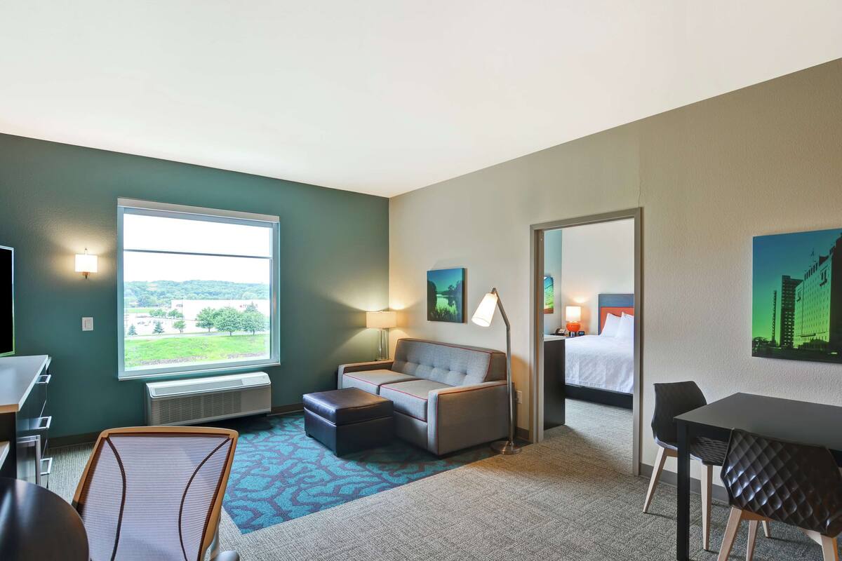 A hotel room with a large window, a sofa, a desk, a chair, and a bed.