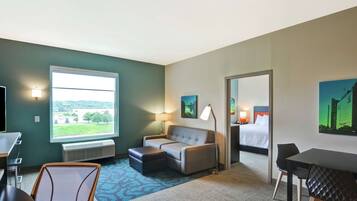 A hotel room with a large window, a sofa, a desk, a chair, and a bed.