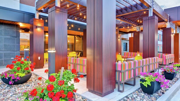 An outdoor seating area with wooden pillars, colorful striped cushions, and potted plants. - Home2 Suites by Hilton Rochester Mayo Clinic Area (Rochester)
