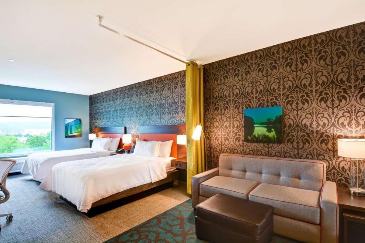 A hotel room with two beds, a sofa, a desk, and a view of the outdoors.