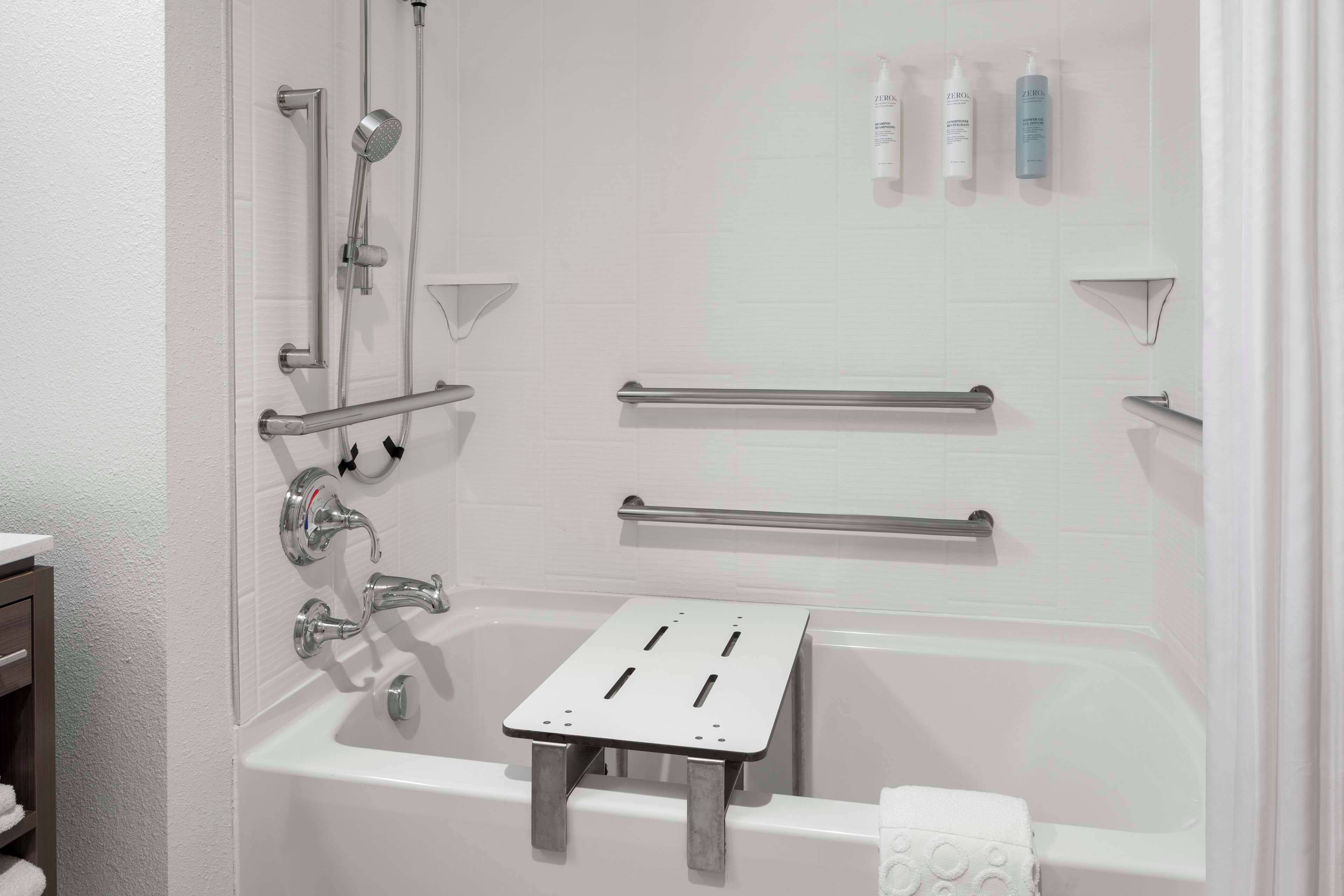 Un baño moderno con ducha a nivel, barras de apoyo y un estante con artículos de aseo.