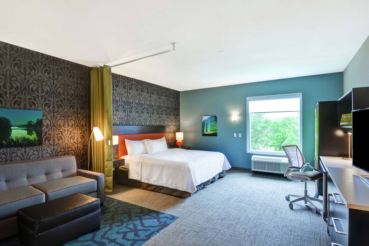 A hotel room with a bed, a sofa, a desk, and a chair.