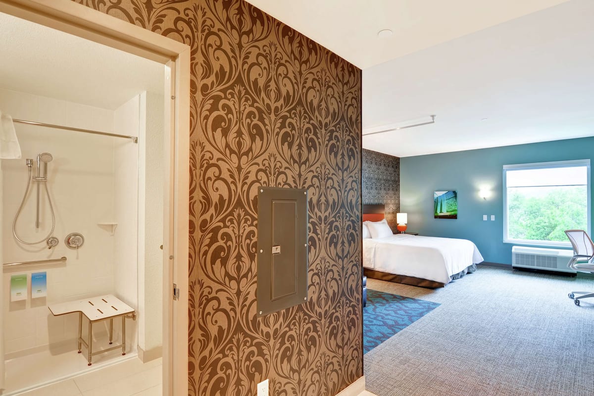 A hotel room with a shower, a bed, a window with a view, and a desk.