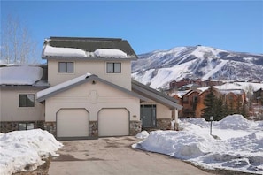Una casa de dos pisos con garaje, rodeada de nieve y un paisaje montañoso.