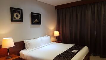 Une chambre d’hôtel avec un grand lit, deux tables de chevet, une commode, une tête de lit, une fenêtre avec des rideaux occultants et deux tableaux encadrés accrochés au mur.