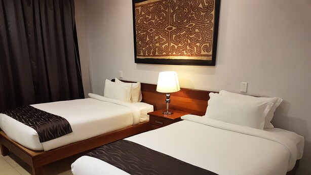 Une chambre d’hôtel avec deux lits simples, une table de chevet avec une lampe et un élément décoratif mural au-dessus des lits.
