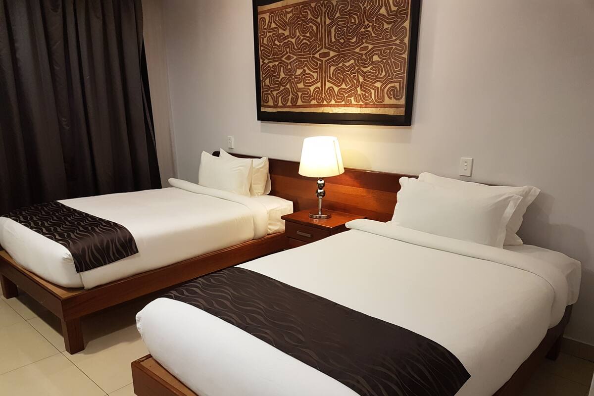 Een hotelkamer met twee enkele bedden, een nachtkastje met een lamp en een decoratief kunstwerk boven de bedden.