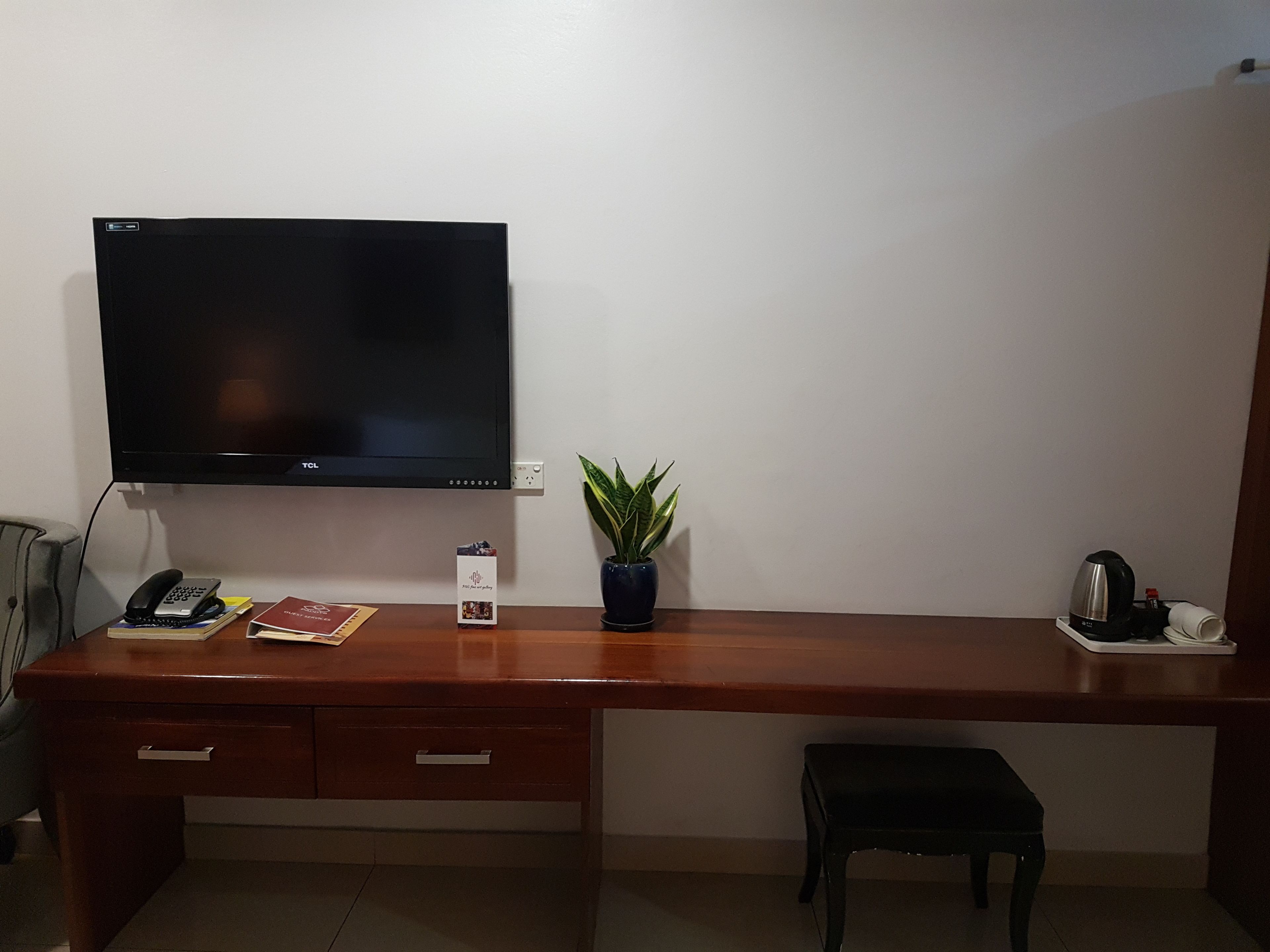 Una scrivania in legno con una TV a schermo piatto, un telefono, una piccola pianta e un bollitore.