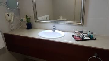 A bathroom with a white sink, a mirror, a telephone, a potted plant, and toiletries on the counter.