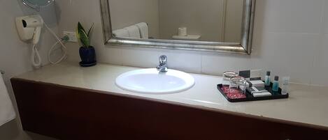 A bathroom with a white sink, a mirror, a telephone, a potted plant, and toiletries on the counter.
