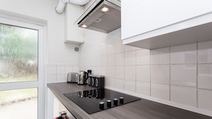 A modern kitchen with a black countertop, white tiles, and a window with frosted glass. - The Northgate (Crawley)
