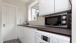 A compact kitchen with a washing machine, a microwave, and a window above the sink. - The Northgate (Crawley)