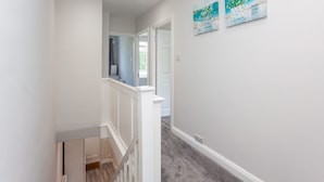 A hallway with a carpeted floor, white walls, and a door leading to another room. There are two paintings on the wall. - The Northgate (Crawley)
