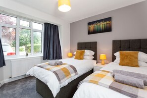 A hotel room with two beds, a cityscape painting, and a window with curtains.