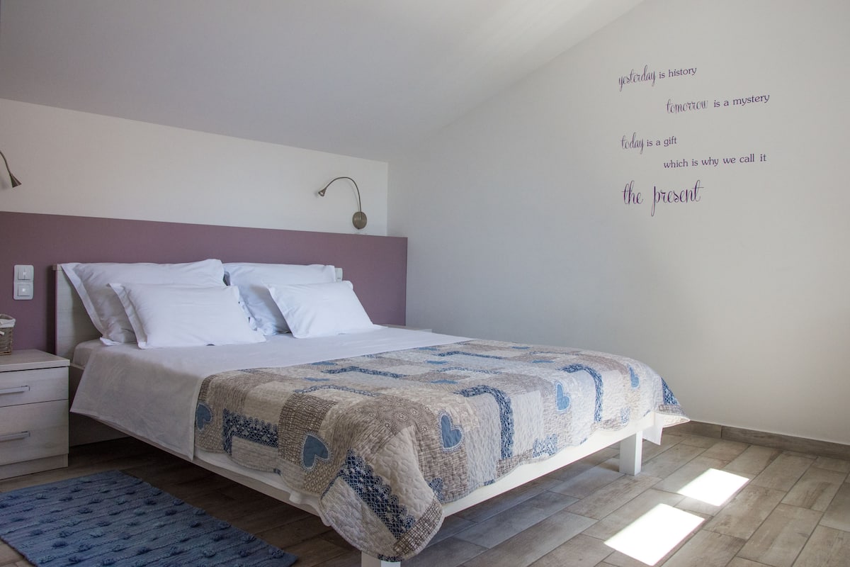 Un dormitorio con cama, mesita de noche, lámpara de pared y alfombra azul.