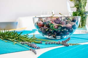 A clear glass bowl filled with cherries and rosemary on a blue tablecloth.