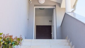 A modern staircase leading to a door, with a security camera above and a small plant to the left. - Apartments Villa Franci (Pag)