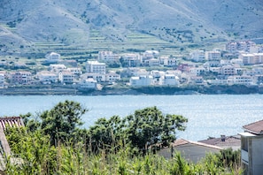 A coastal town with buildings along the shoreline, a clear view of the sea, and hills in the background.