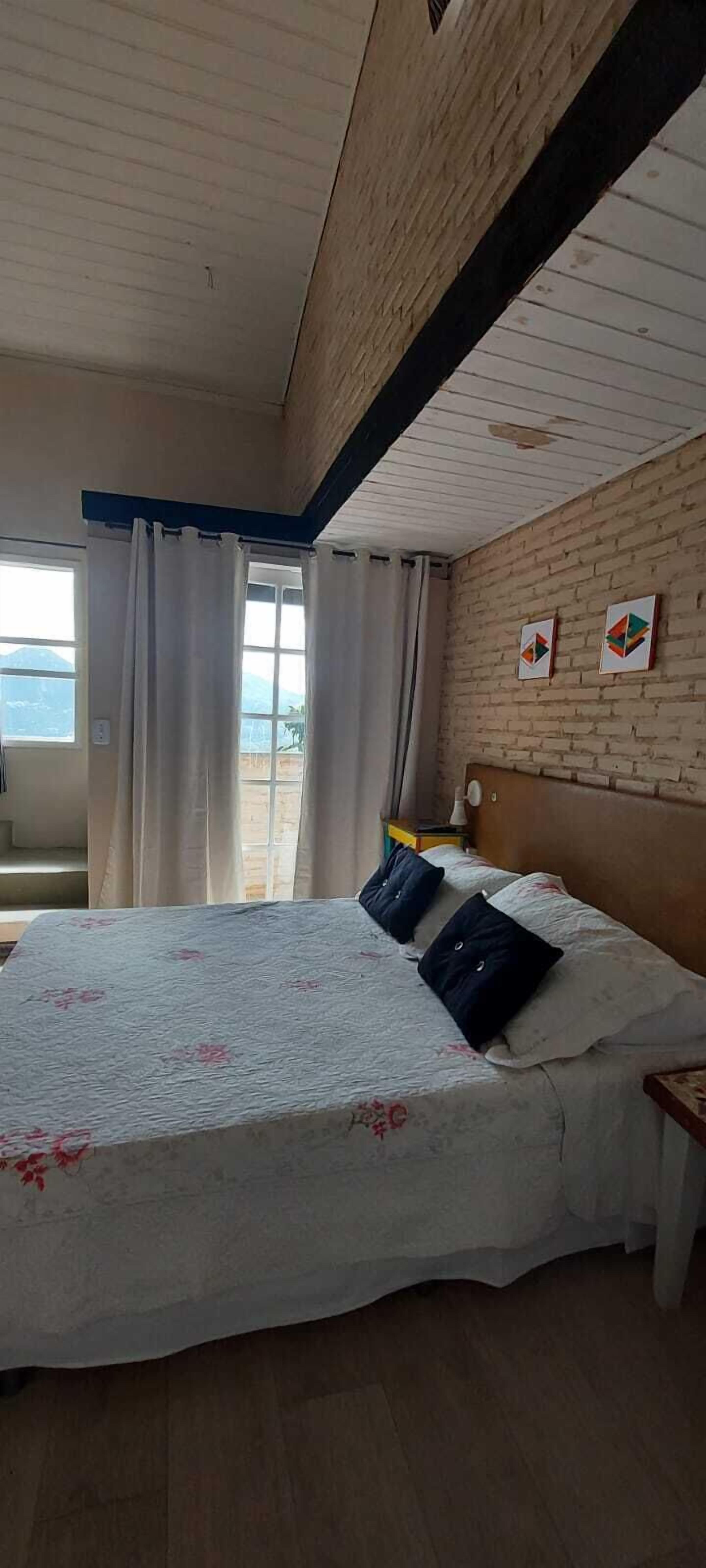 Una habitación de hotel con una cama grande, un cabecero de madera, una ventana con cortinas y una pared de ladrillo.
