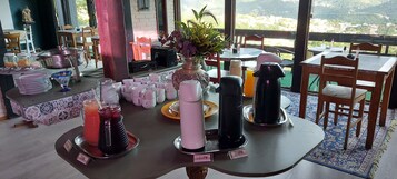 Montaje de un bufé de desayuno con diversos platos y bebidas, un jarrón con flores y vistas al paisaje.