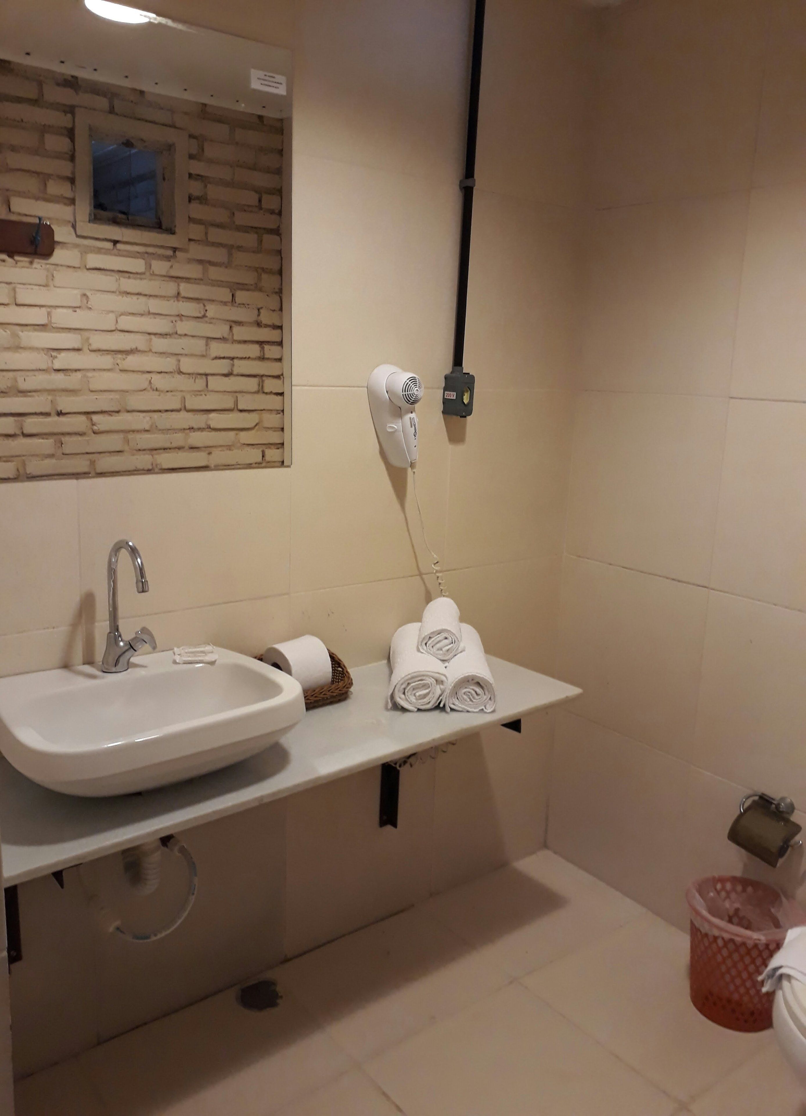 A bathroom with a white sink, a hairdryer, a towel rack, and a shower area.