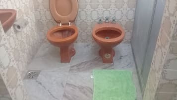 Un baño con dos inodoros, piso de mármol, papel tapiz estampado y una toalla verde.