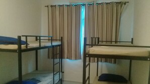 Ein Schlafsaalzimmer mit zwei Etagenbetten, einem Fenster mit Vorhängen und einem Heizkörper.