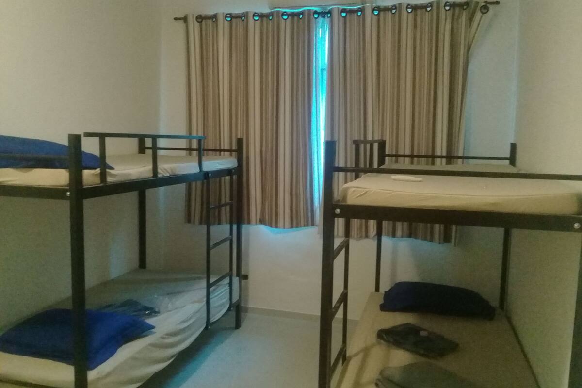 A dormitory room with two bunk beds, a window with curtains, and a radiator.
