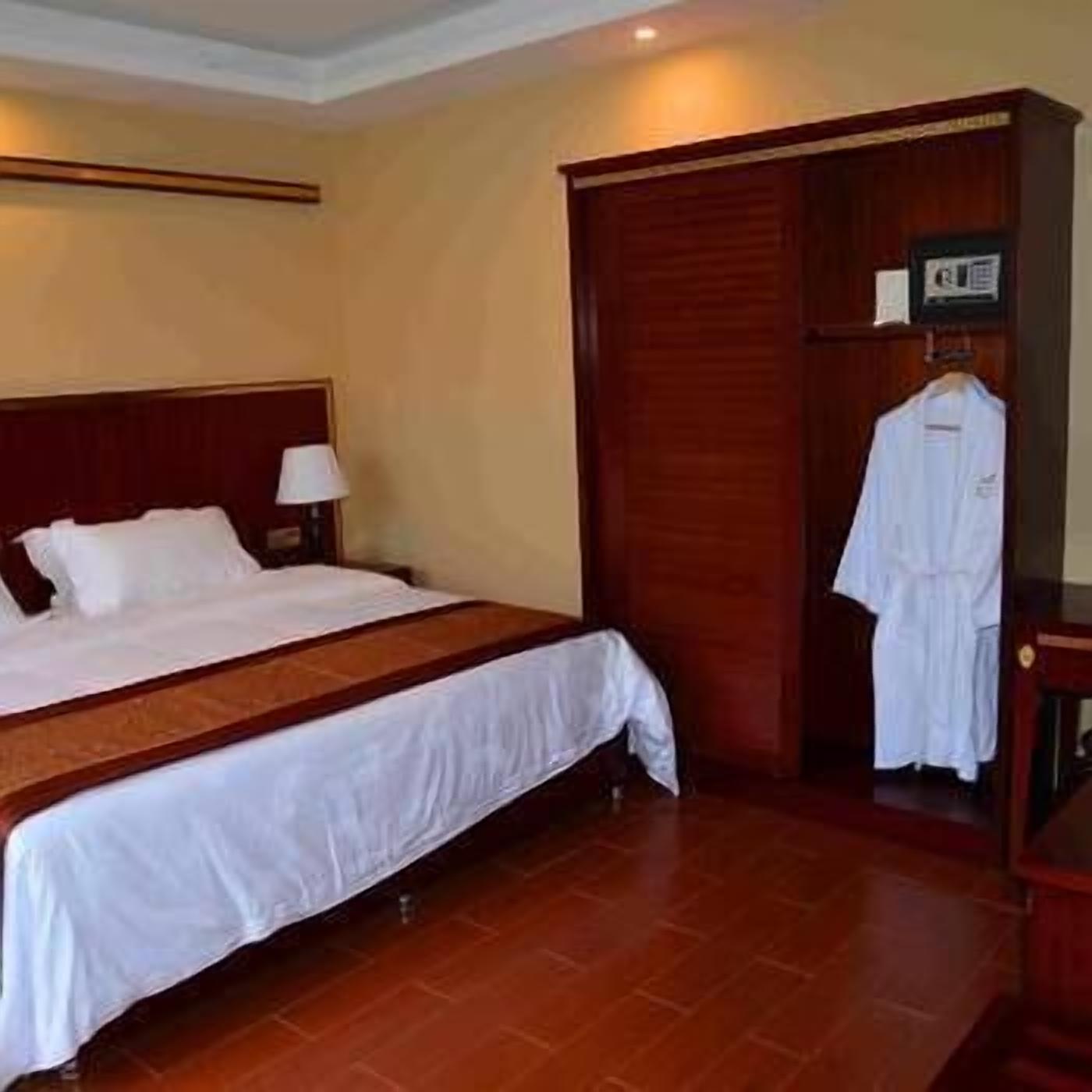 A hotel room with a large bed, a wooden wardrobe, and a robe hanging on the door.