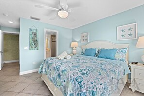 A bedroom with a bed, a nightstand, a ceiling fan, and a door leading to another room.