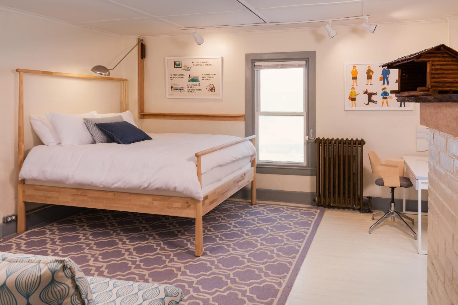 A bedroom with a wooden bed, a desk, a chair, a radiator, and a window.