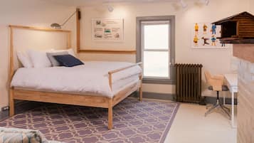 A bedroom with a wooden bed, a desk, a chair, a radiator, and a window.