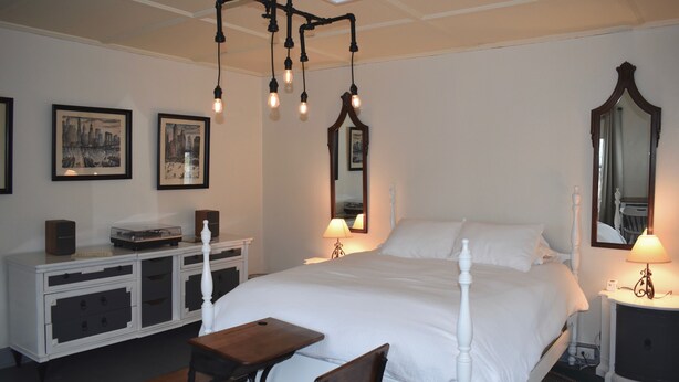 A neatly arranged bedroom with a large bed, bedside tables, a mirror, and a chandelier. - The Deers Head Inn (Elizabethtown)