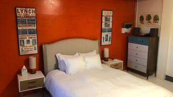 A hotel room with a large bed, a nightstand with a lamp, a dresser, and two posters on the wall.