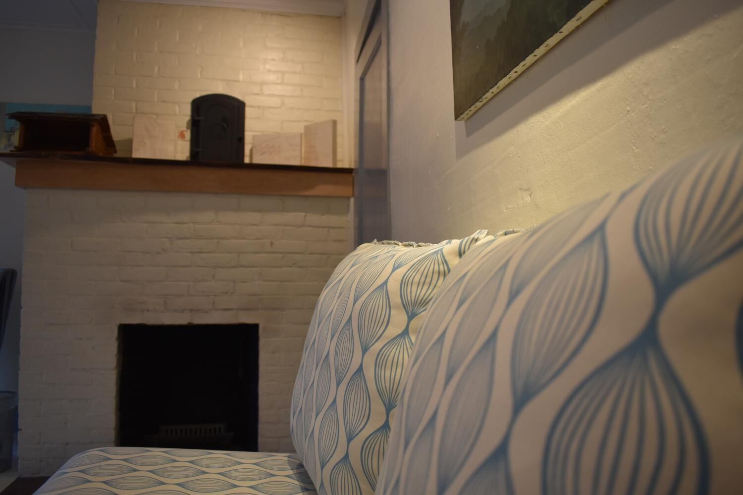 Una habitación con chimenea de ladrillo blanco, repisa de madera encima y sofá estampado.