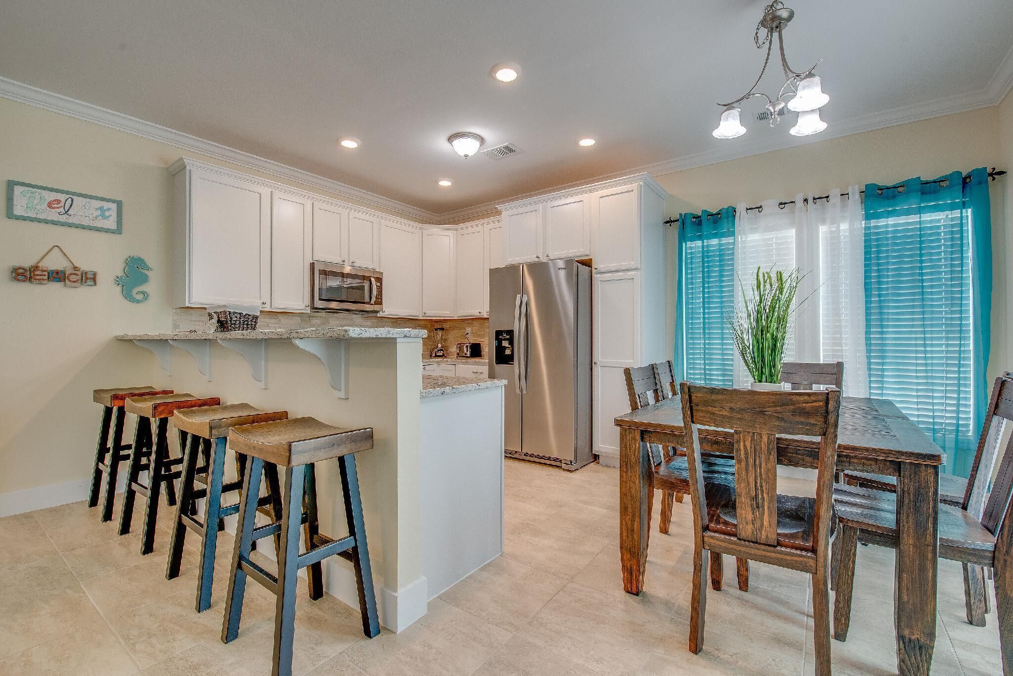 A kitchen with white cabinets, a stainless steel refrigerator, a wooden dining table, and bar stools.