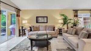 A living room with a beige sofa, a glass coffee table, and a large window with curtains. - VP2522DC - Pool Home - Conservation Views - Sleeps Up to 8 (Kissimmee)