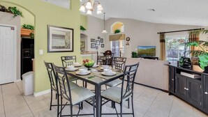 A dining area with a table set for four, surrounded by chairs, a chandelier, and a view of a kitchen and living area. - VP2522DC - Pool Home - Conservation Views - Sleeps Up to 8 (Kissimmee)