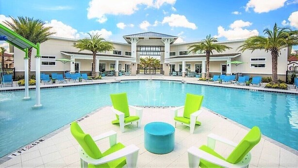 A pool area with a central seating arrangement, palm trees, and a building with a flat roof and large windows. - VP2522DC - Pool Home - Conservation Views - Sleeps Up to 8 (Kissimmee)