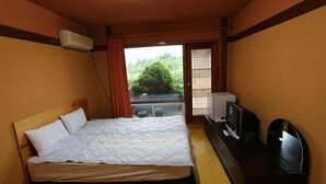 Ett hotellrum med en säng, en tv och ett fönster med utsikt över grönområden.