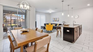 A modern kitchen with a central island, a dining area with a wooden table and chairs, and a living area with a sofa and yellow chairs. - Private Pool-Upgraded Interior-Poolside Bar (Davenport)