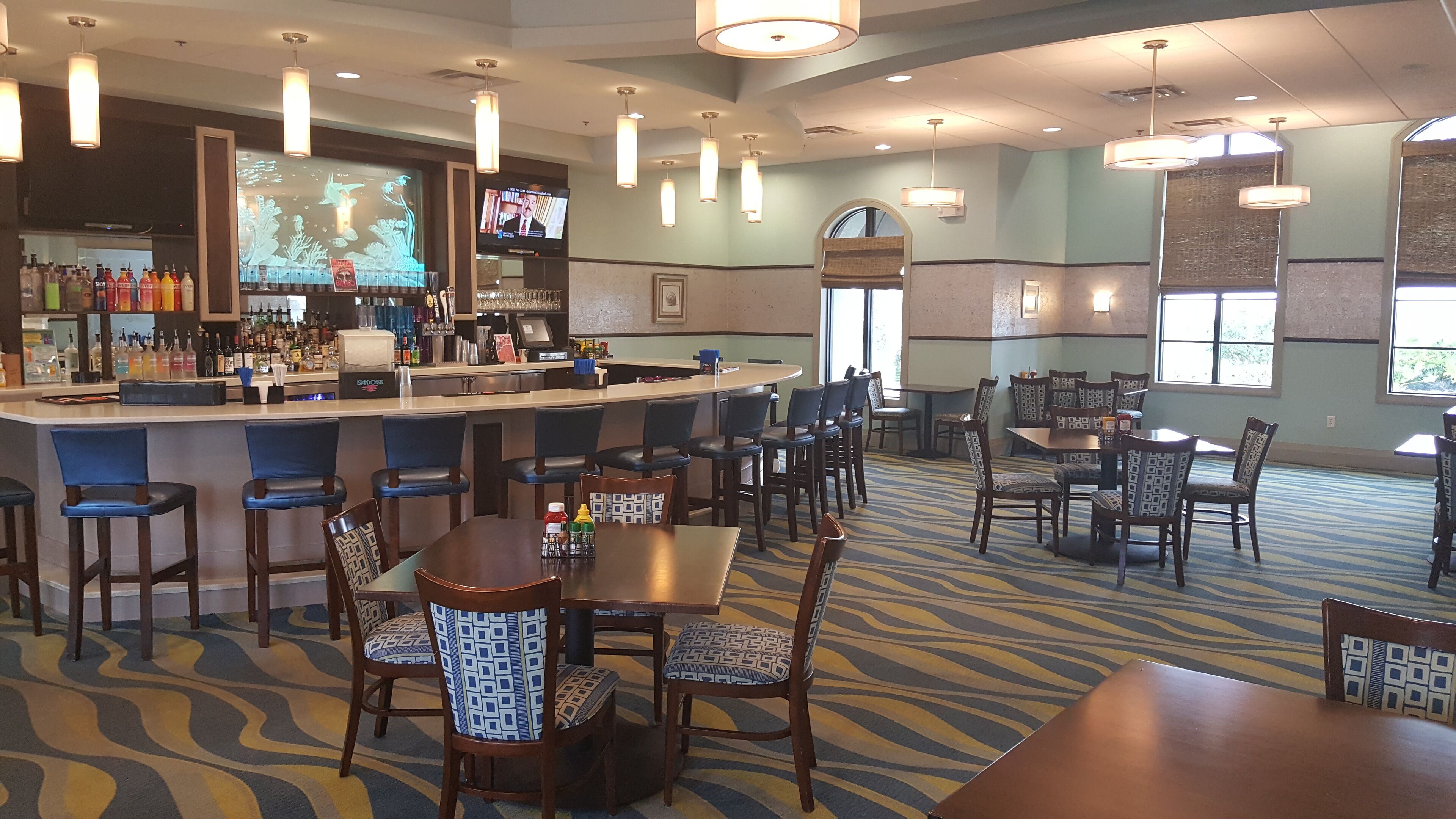 A bar area with a counter, bar stools, and a television screen displaying a news program.