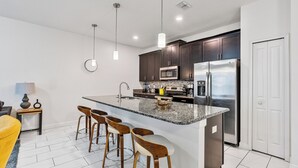 A modern kitchen with dark cabinets, stainless steel appliances, a granite countertop, and bar stools. - Private Pool-Upgraded Interior-Poolside Bar (Davenport)