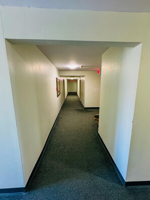 A corridor with a carpeted floor, white walls, and a ceiling light.