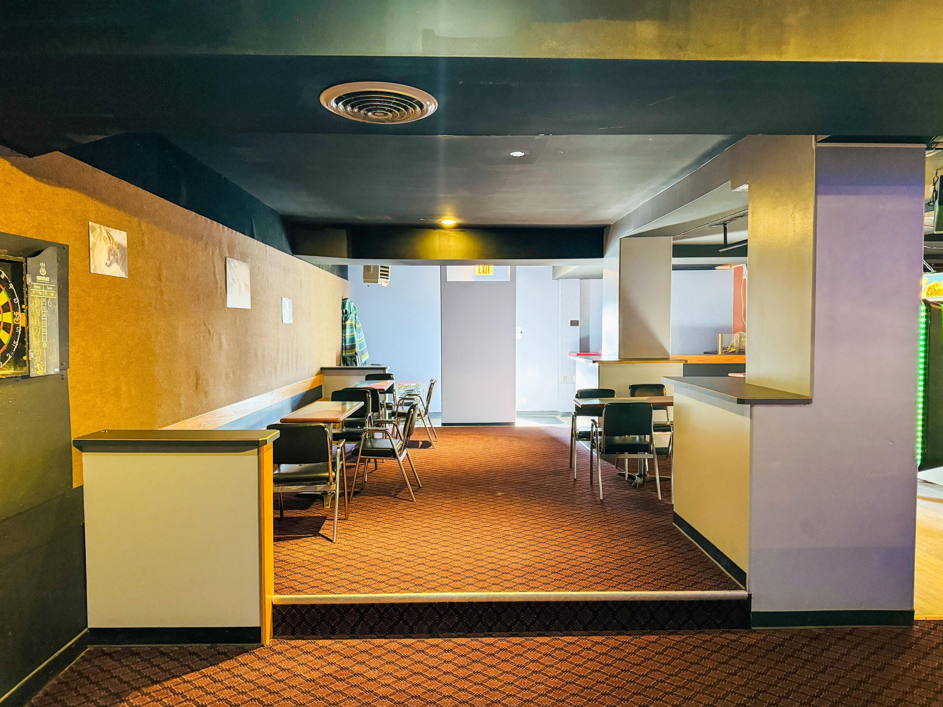 A modern interior with a patterned carpet, tables, chairs, and a vending machine.