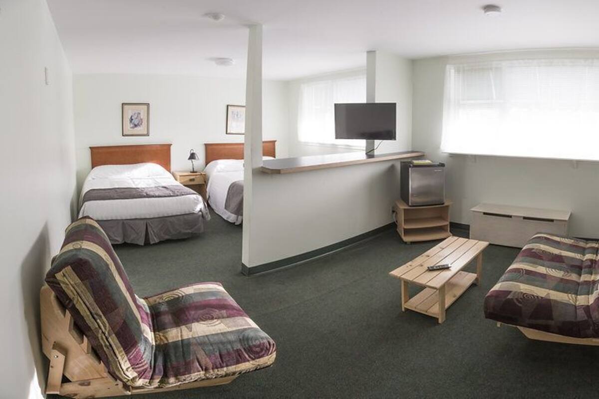 Ein kleines Hotelzimmer mit zwei Betten, einem kleinen Schreibtisch mit Fernseher, einer Sitzecke und einem Sessel.
