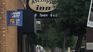 Vista de la calle con un cartel que dice 'Assissip Inn' y un cajero automático 'Laser Cash'.